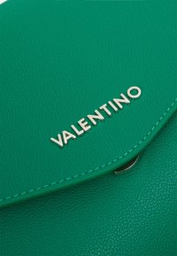Clutch de cuero texturizado verde con cierre de solapa, que presenta el logotipo plateado "VALENTINO". Detalles de costura sutiles acentúan los bordes.