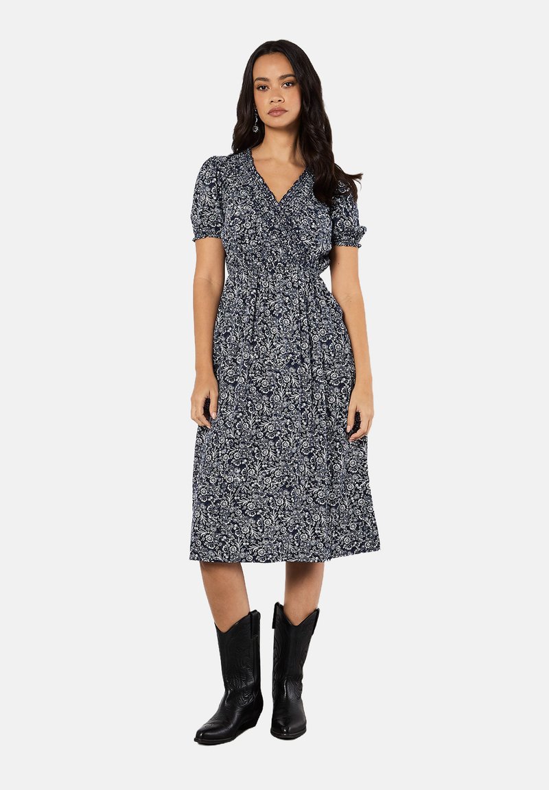 Marineblaues Blumenkleid mit kurzen Puffärmeln, geraffter Taille und knielangem Rock; kombiniert mit schwarzen Cowboyboots.