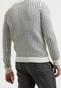 Pull en maille crème avec motif pied-de-poule noir. Comprend des poignets et un ourlet côtelés. Mélange de coton avec une finition texturée.