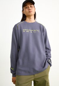 Grå langærmet sweatshirt med tekstureret stof, gule accenter og trykte logoer. Har ribbet krave og manchetter samt en afslappet pasform.