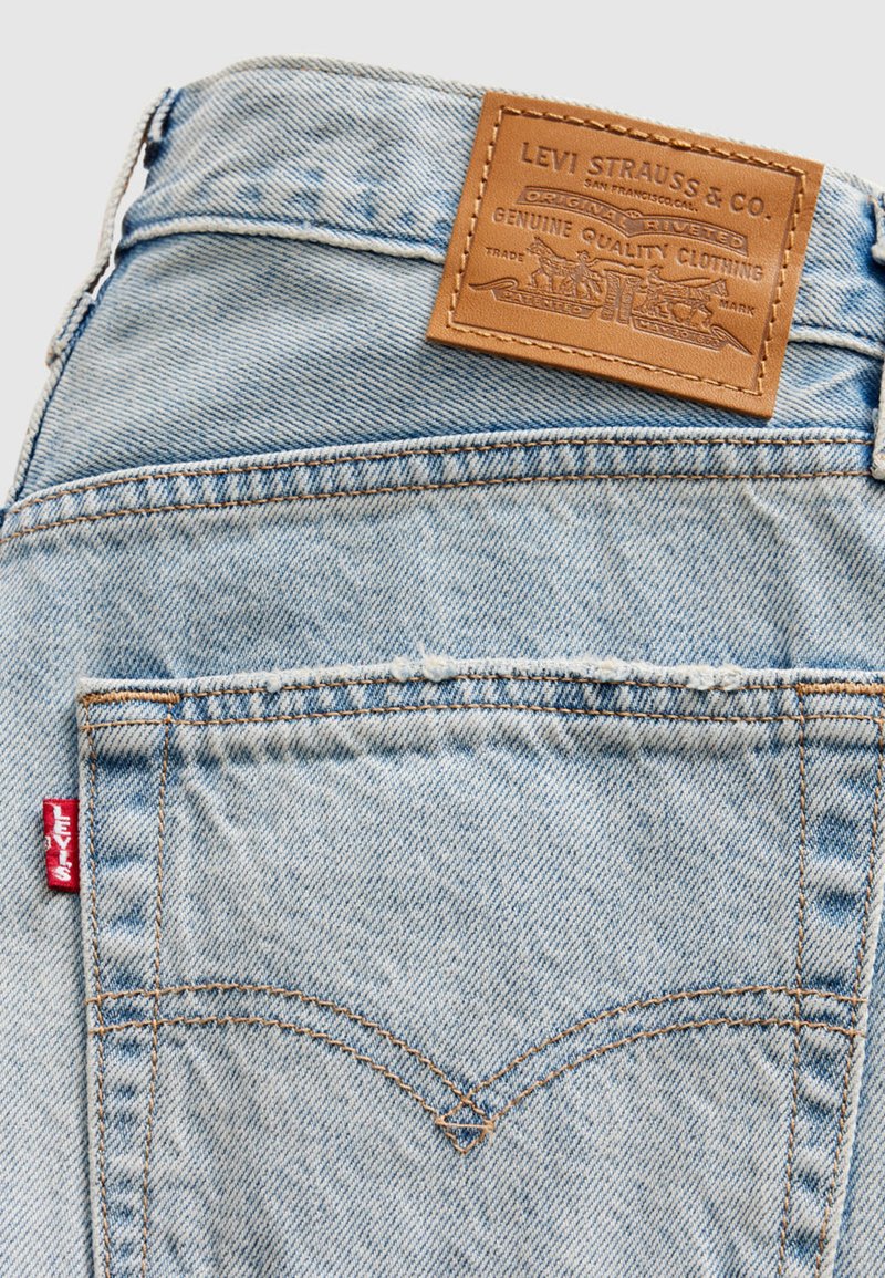 Jean en denim bleu clair avec une pièce en cuir portant l'étiquette "Levi Strauss & Co." et une étiquette rouge sur la poche arrière. Présente un design de couture classique.