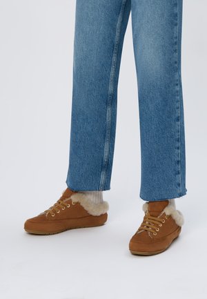 Chaussures en suède marron avec bordure en fausse fourrure, devant à lacets et semelle en caoutchouc texturé. Portées avec un jean bleu clair à jambes larges et des chaussettes claires.