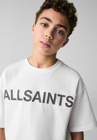 Vit t-shirt med fet svart "ALLSAINTS" text. Tillverkad av mjukt tyg, med korta ärmar och en avslappnad passform.
