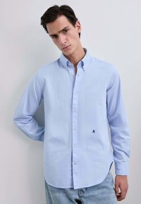 Chemise boutonnée bleu clair à manches longues, avec col et accent logo discret. Fabriquée en coton, elle présente une coupe décontractée et un ourlet droit.