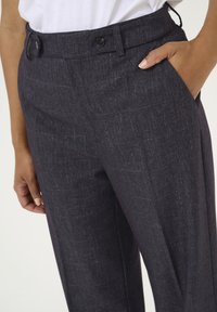 Dark gray trousers made from textured fabric, featuring a mid-rise waist, a button closure, and side pockets. Slender fit design.