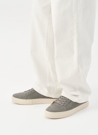 Γκρι σουέτ αθλητικά παπούτσια με κρεμ καουτσούκ σόλες, με λεία υφή και κλασικό σχέδιο με κορδόνια, συνδυασμένα με λευκά παντελόνια.