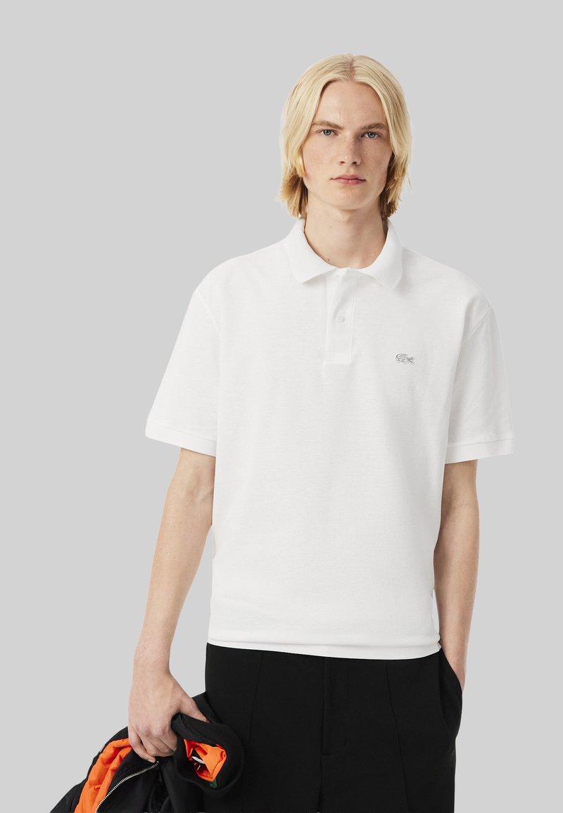 Vit polo skjorta i mjukt tyg, med klassisk krage, korta ärmar och en liten broderad logotyp på bröstet.