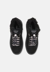 Sneaker in suede nero con un collare morbido e testurizzato, lacci stampati e suola in gomma. Brand visibile sulla linguetta e sui lacci.