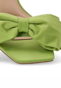 Sandal de tacón verde satinado con un gran lazo en la parte frontal. Presenta una punta cuadrada y una textura suave, con un diseño minimalista.