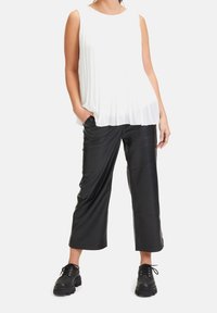 Vit plisserad ärmlös topp kombinerad med svarta fusk läder cropped-byxor och svarta snörstövlar med kraftig sula, vilket skapar en kontrast i texturer.