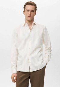 Camisa blanca de manga larga con finas rayas verticales, con cuello abotonado y corte recto. Textura lisa y detalles mínimos.