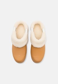 Scarpe slip-on beige con un morbido colletto e rivestimento in pile color crema, dotate di una punta arrotondata e suola testurizzata.