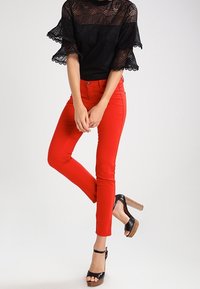 Røde tætsiddende bukser lavet af strækstof, kombineret med en sort blonde top med flæseærmer. Sorte platformsandaler med træhæl.