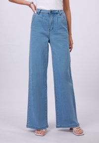 Svijetloplave široke traperice napravljene od denima, s visokim strukom, prednjim naborima, zatvaranjem na gumb i suptilnom teksturom kroz cijelu površinu.