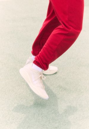 White athletic shoes with a smooth texture and prominent sole, worn with red joggers featuring a gathered ankle hem.