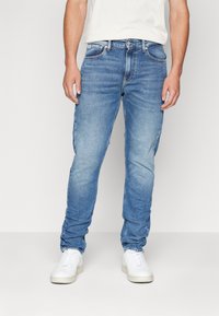 Ljust blå denimjeans med slim fit, som har en femficksdesign och subtila blekningar. Återfinns med vita sneakers.