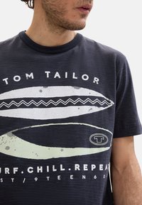 Marineblå bomulds t-shirt med stribemønster, rund halsudskæring og dristigt grafisk design med surfer-tema og logo-tekst.