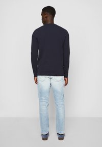 Marineblaues Longsleeve-Shirt mit rundem Ausschnitt, kombiniert mit hellblauen Jeans. Die Textur ist glatt und der Schnitt ist lässig und bequem.