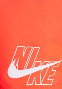 Narancssárga Nike sportruha sima textúrával, kiemelkedő fehér logóval és bátor feliratozással. Egyszerű, letisztult dizájn.
