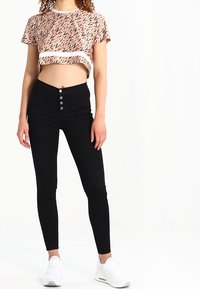 Top corto de manga corta en rosa con patrón geométrico; pantalones negros de cintura alta con cinco botones; zapatillas deportivas blancas.