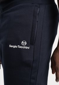 Marina joggers i texturerat material, med sidofickor och en vit "Sergio Tacchini"-logotyp på lårområdet.