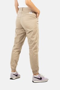 Pantalones cargo beige con cintura elástica y bolsillos laterales, textura suave y puños elásticos, combinados con zapatillas ligeras en púrpura y negro.