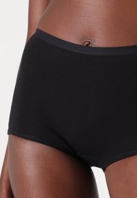 Black cotton hipster underwear with a smooth texture, featuring a soft, elastic waistband and stitched detailing at the edges.