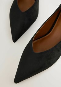 Svarta mocka ballerinas med spetsig tå och V-formad design. Insidan har en slät brun foder som ger en elegant och strukturerad siluett.