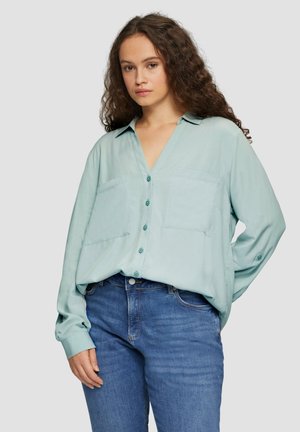 Licht turquoise blouse met knopen, een V-hals, twee voorzakken, lange mouwen en een relaxed fit, gecombineerd met blauwe jeans.