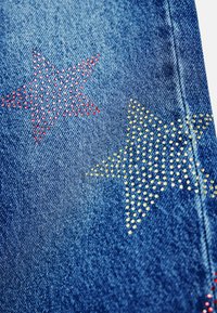 Denimtyg med två stjärnformer, en röd med rhinestones och en gul med rhinestones, på en blå bakgrund.