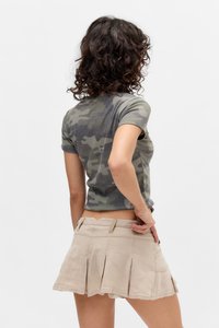 Chemise grise à motifs camouflage à manches courtes associée à une jupe plissée beige avec des poches latérales et un ourlet ondulé. Vue arrière.