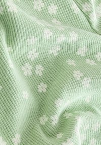 Tissu côtelé vert clair avec des motifs de fleurs blanches, offrant une texture douce et une variation de profondeur et de plis.