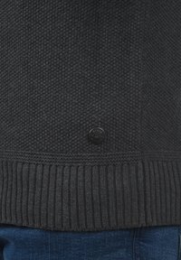 Dunkelgrauer Pullover mit einer strukturierten Strickmusterung, geripptem Saum und einem runden schwarzen Logo-Knopf an der Seite. Material aus Baumwollmischung.