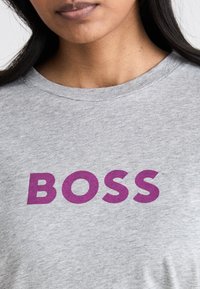 Pilkas medvilnės marškinėliai su ryškiu purpuriniu užrašu "BOSS" ant krūtinės, su klasikiniu apvaliu kaklu.