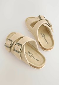 Beige Wildledersandalen mit zwei verstellbaren Riemen, silbernen Schnallen, offenen Seiten und einer konturierten Fußbett. Strukturierte Außensohle für besseren Halt.