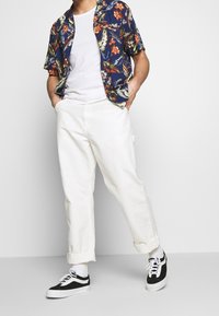 Paita lyhyillä hihoilla kukkakuosilla tummansinisenä, valkoiset puuvillahousut käärittyine lahkeineen ja mustat Vans-tennarit valkoisilla nauhoilla.