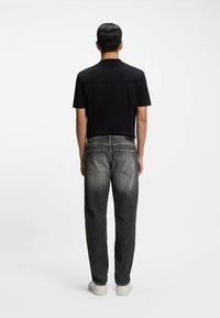 Czarna koszula z krótkim rękawem w połączeniu z ciemnoszarymi prostymi jeansami. Jeansy mają wyblakły odcień i dwie tylne kieszenie. Całość uzupełniają białe buty.