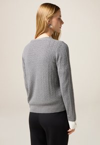 Grau gerippter Strickpullover mit rundem Halsausschnitt und schmalem Saum. Er hat eine weiche Textur und lange Ärmel über einer schwarzen Hose.
