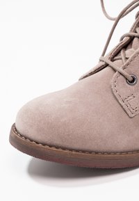 Light brown suede ankle boot with a rounded toe, lace-up front, and a rubber sole. Includes stitched detailing around the ankle area.