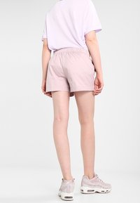 Helle rosa Shorts mit elastischem Bund und glatter Textur, kombiniert mit einem lockeren lilafarbenen T-Shirt und pinken Sportschuhen. Rückansicht.