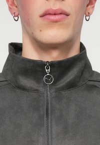 Hall grey fliisist tõmblukuga jakk, millel on kõrge krae, hõbedane tõmblukukäepide logo ja minimaalsed õmblusdetailid.