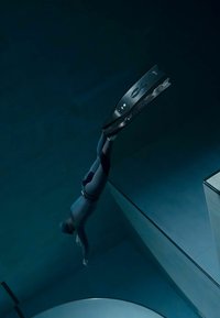 Zwarte duikvinnen met geperforeerd oppervlak, gedragen door een duiker in een blauw wetsuit, die opstijgt in donker water, met zichtbare geometrische rand van het zwembad.