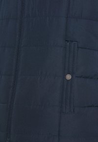 Navy blue puffer jacket section with a textured, quilted design, a central zipper, and a snap button pocket detail on the left side.