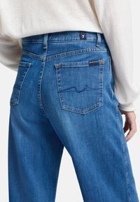 Jeans in denim blu a vita alta con una vestibilità rilassata, dotati di doppie tasche posteriori e dettagli di cucitura discreti. Texture liscia, design classico.