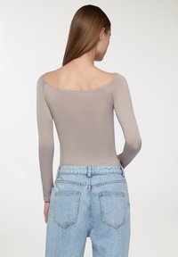 Bodysuit z długim rękawem, odsłoniętymi ramionami w jasnym taupe, zestawiony z jeansami o wysokim stanie w jasnym niebieskim kolorze z tylnymi kieszeniami. Gładka faktura.