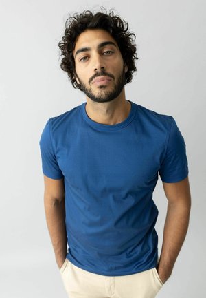 Blaues Baumwoll-T-Shirt mit kurzen Ärmeln, rundem Ausschnitt, glatter Textur und figurbetontem Design, kombiniert mit hellen Hosen.