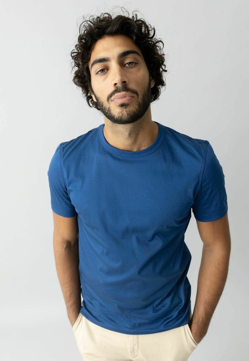 Zila kokvilnas t-kreklu ar īsām piedurknēm, apaļo kakla izgriezumu, gludu tekstūru un pieguļošu dizainu, apvienots ar gaišām biksēm.