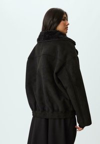 Crna umjetna sued jakna s puhastim, teksturiranim ovratnikom. Oversized dizajn s rebrastim donjim dijelom i manžetama. Nema vidljivog hardvera ili uzoraka.