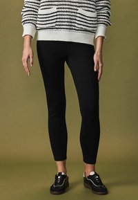 Black leggings made of stretchy fabric, featuring a slim fit. Paired with a knit striped sweater and black sneakers with white accents.