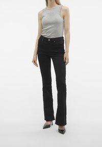 Black flared jeans with a high waist, paired with a light gray sleeveless top. Material appears smooth; denim features minimal detailing.
